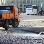 Impregnacja i pielęgnacja betonu architektonicznego na zewnątrz przez cały rok Pracownik miasta myje ulicę wodą z węża w słoneczny dzień