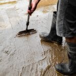 Pracownik w kaloszach czyści betonową posadzkę szczotką